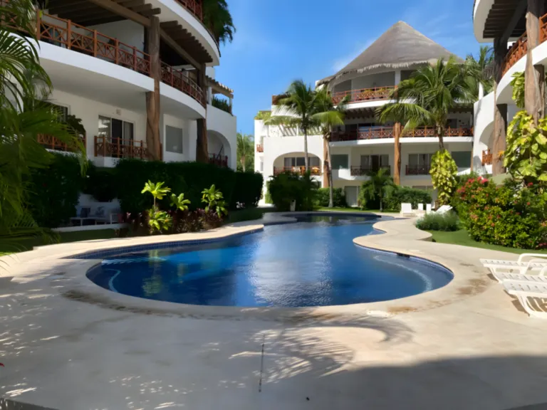 Disfruta de una piscina tranquila y soleada en un entorno tropical en Playa del Carmen Piscina tropical rodeada de palmeras y jardines en una residencia de Playa del Carmen